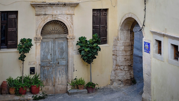 A narrow street with a traditional stone building, a wooden door, and potted plants. - Family home w. yard in Beating Heart of Old Town (Chania)