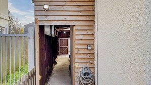 A narrow wooden pathway leading to a barn-like structure with a metal gate and a security device.
