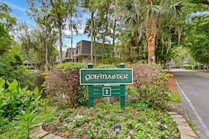 A golf course sign with a number '1' indicating the first hole, surrounded by lush greenery and a pond.