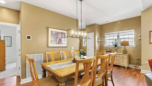 Un comedor con una mesa y sillas de madera, una lámpara colgante y un ventanal con persianas.