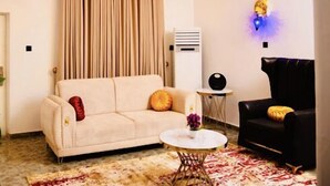 A living room with a beige sofa, a black armchair, a round coffee table, and a chandelier. - Boston Residence Limited  (Enugu)
