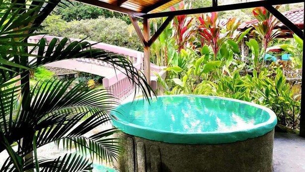 Ein Whirlpool unter einer Holzpergola, im Hintergrund üppiges Grün.