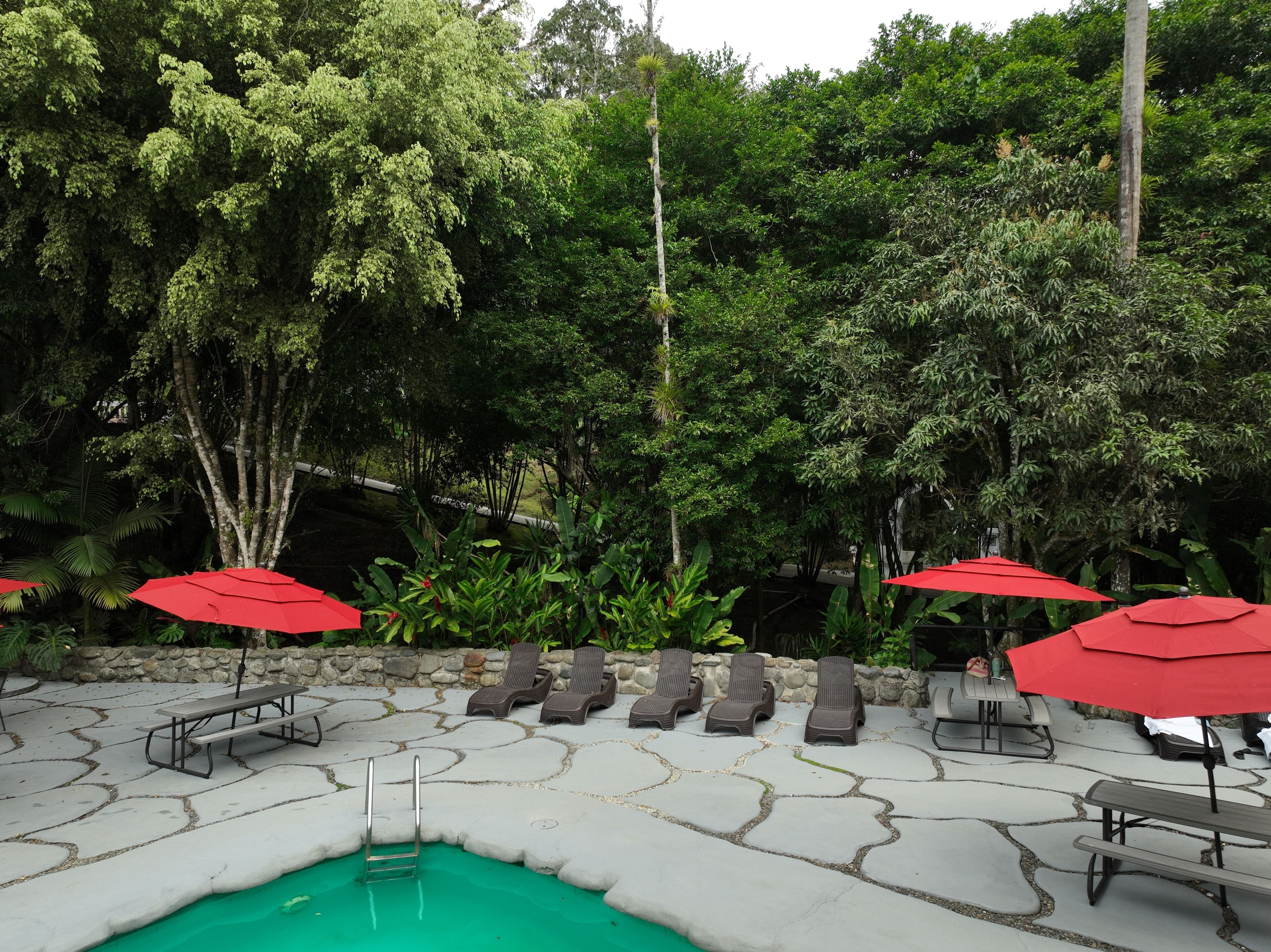 A poolside area with lounge chairs, red umbrellas, and a stone-tiled deck.