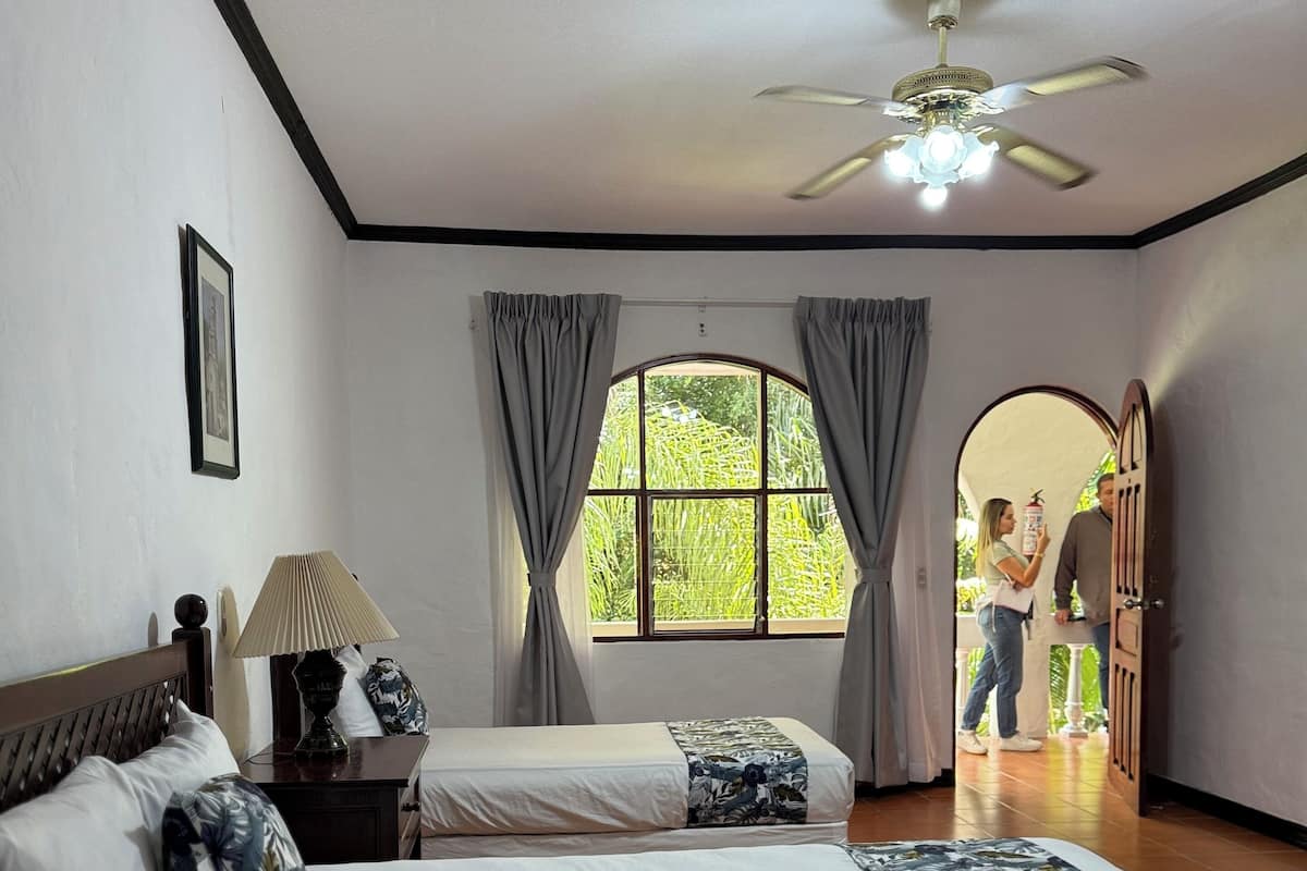 A bedroom with a large bed, two bedside tables, a ceiling fan, and a window with curtains.