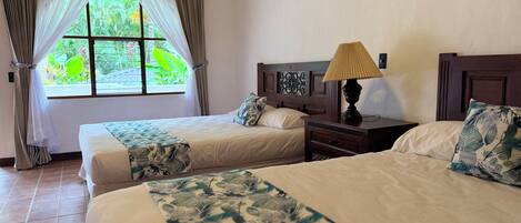 A room with two beds, a nightstand with a lamp, and a window with curtains.