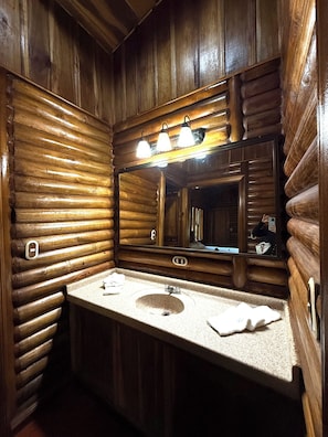 A wooden cabin-style bathroom with a sink, mirror, and three light fixtures above the mirror.