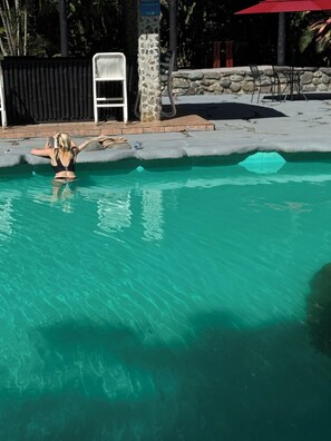 A swimming pool with clear water, a stone pillar, and a white chair.