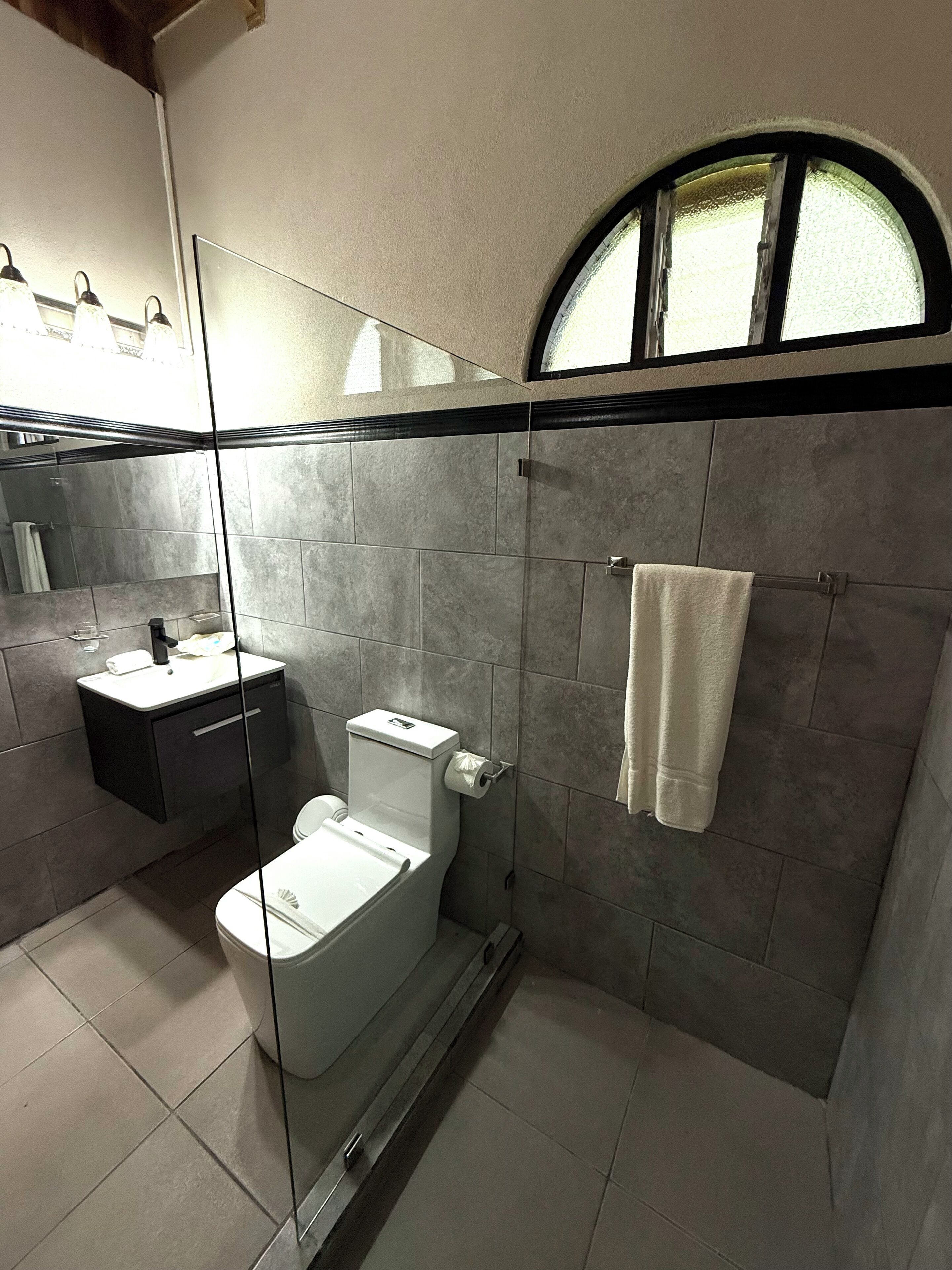 Un baño moderno con cabina de ducha de vidrio, inodoro, lavabo y una toalla colgada en un perchero.