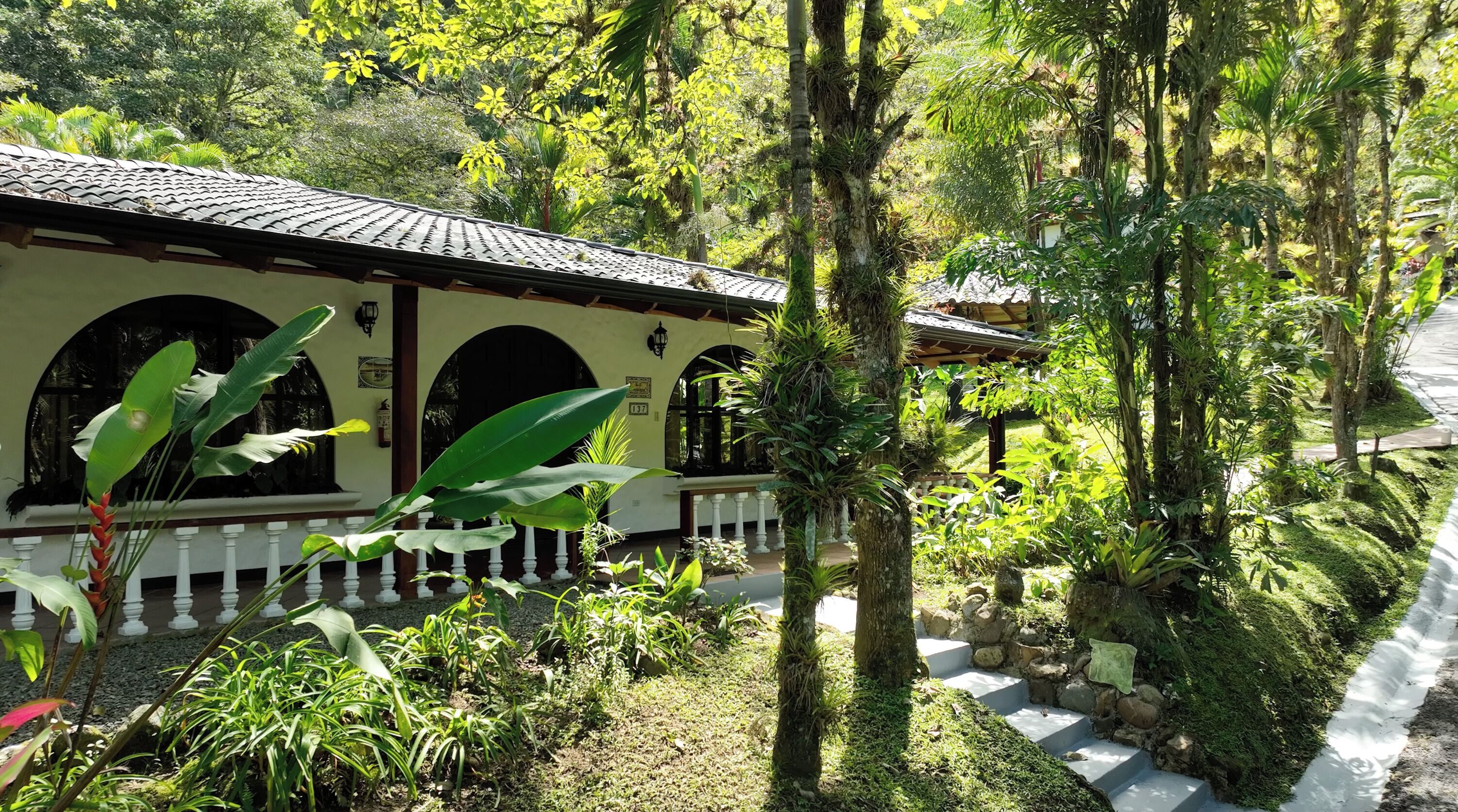 A traditional building with a tiled roof, surrounded by lush greenery and a stone pathway.