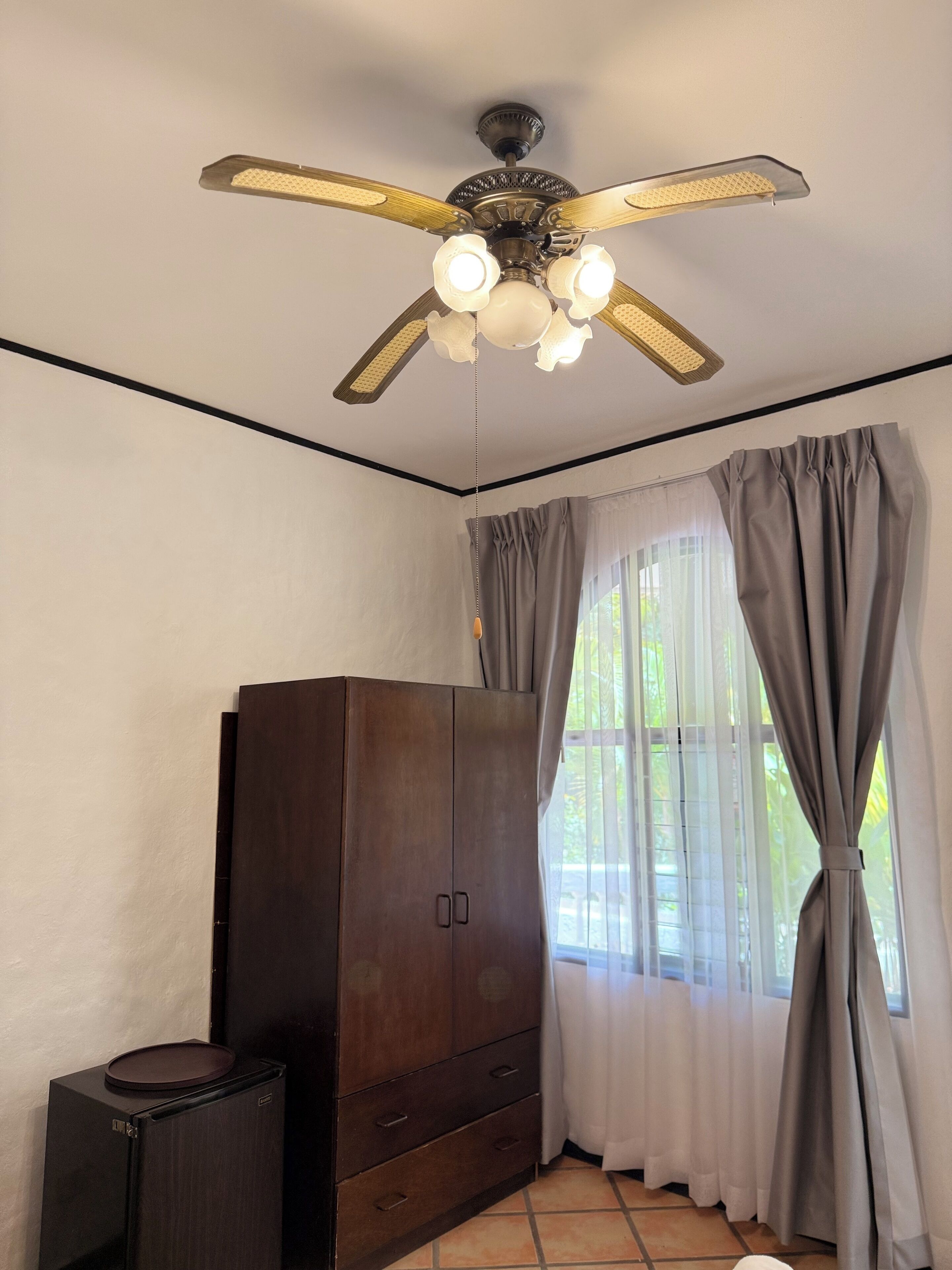 A room with a ceiling fan, a wardrobe, and a window with curtains.