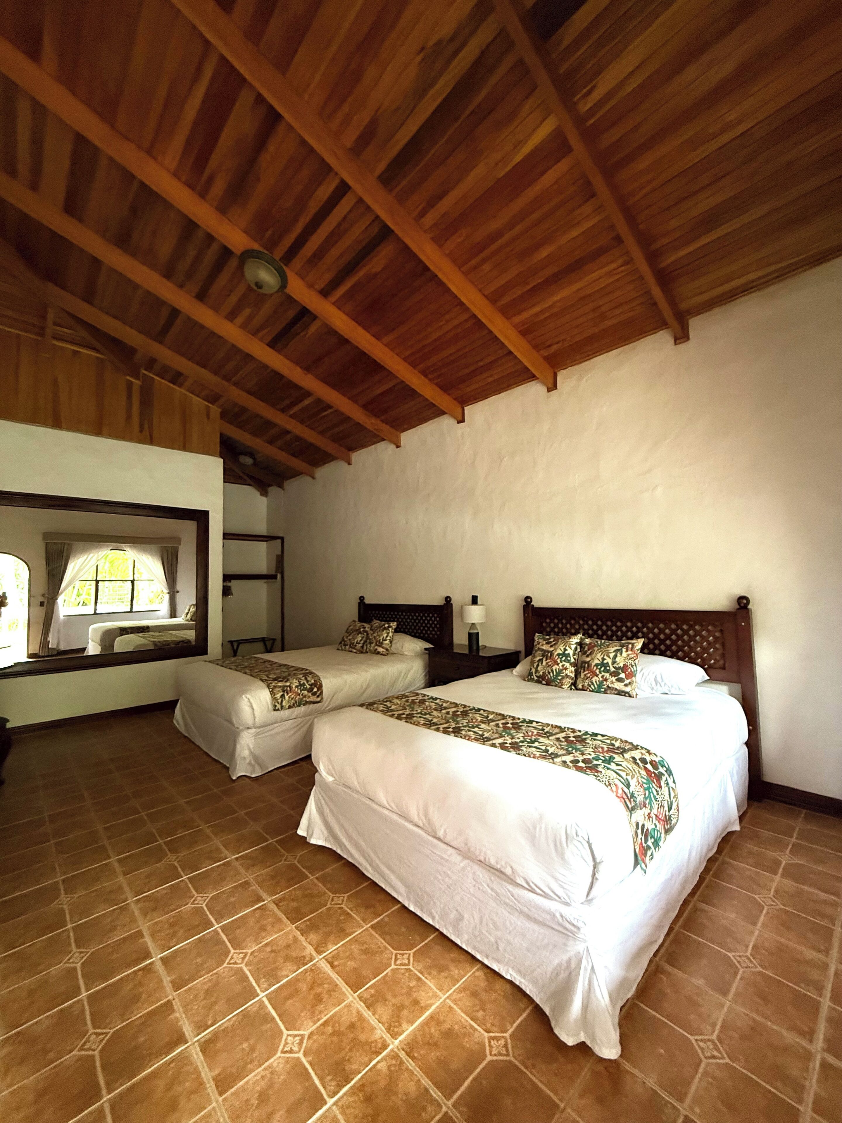 Une chambre avec deux lits, une fenêtre avec des rideaux et un plafond en bois.