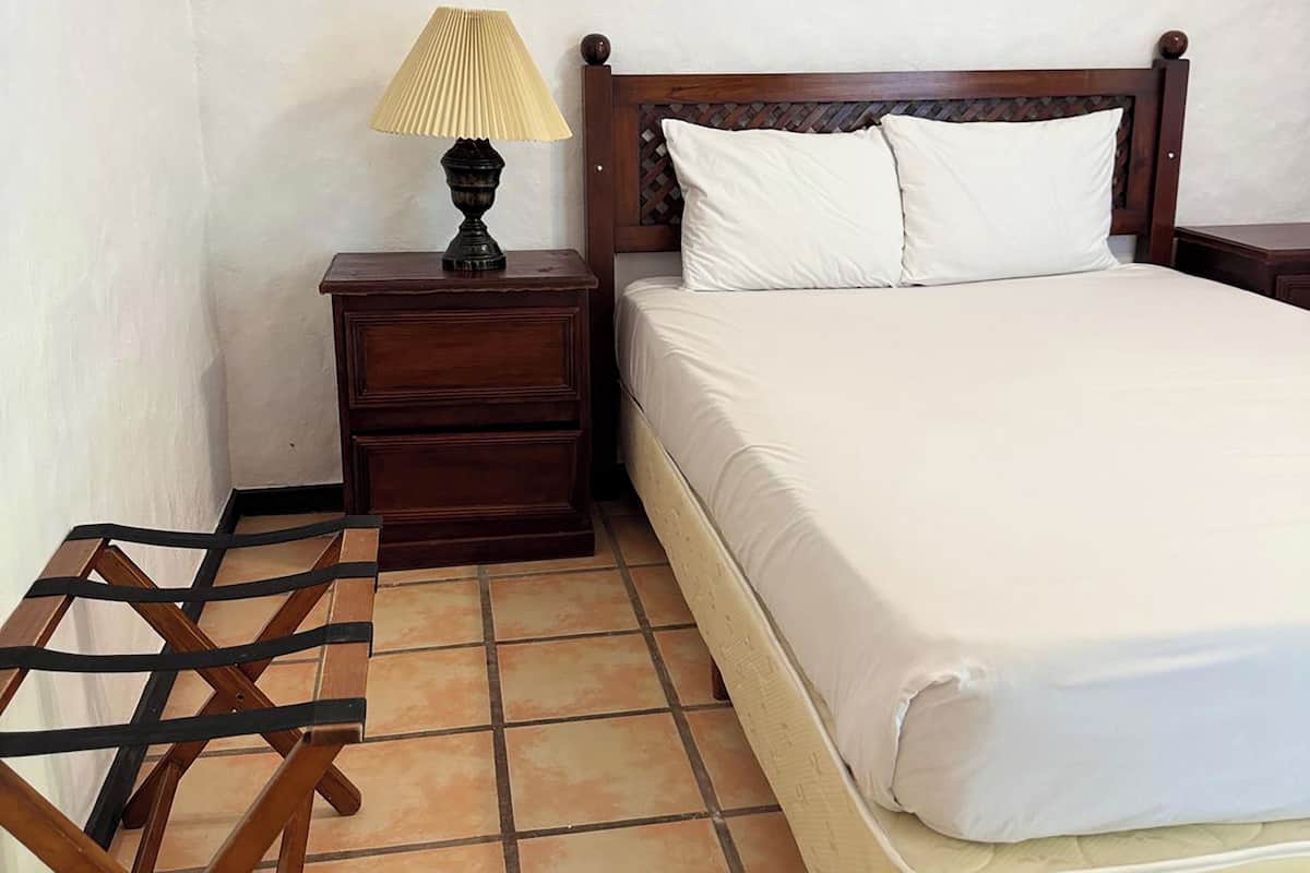 A bedroom with a wooden bed, a nightstand with a lamp, and a wooden chair.