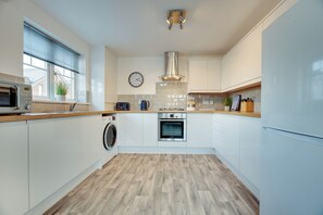 A modern kitchen with white cabinets, a built-in oven, a microwave, and a washing machine. - Cooksons Apartments (North Shields)
