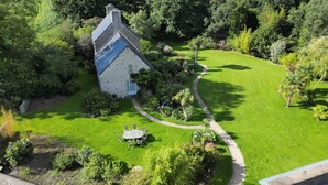 An aerial view of a stone house with a well-maintained lawn and a garden path leading to a seating area.