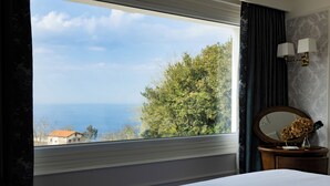 Una camera d'albergo con un'ampia finestra vista mare e alberi.