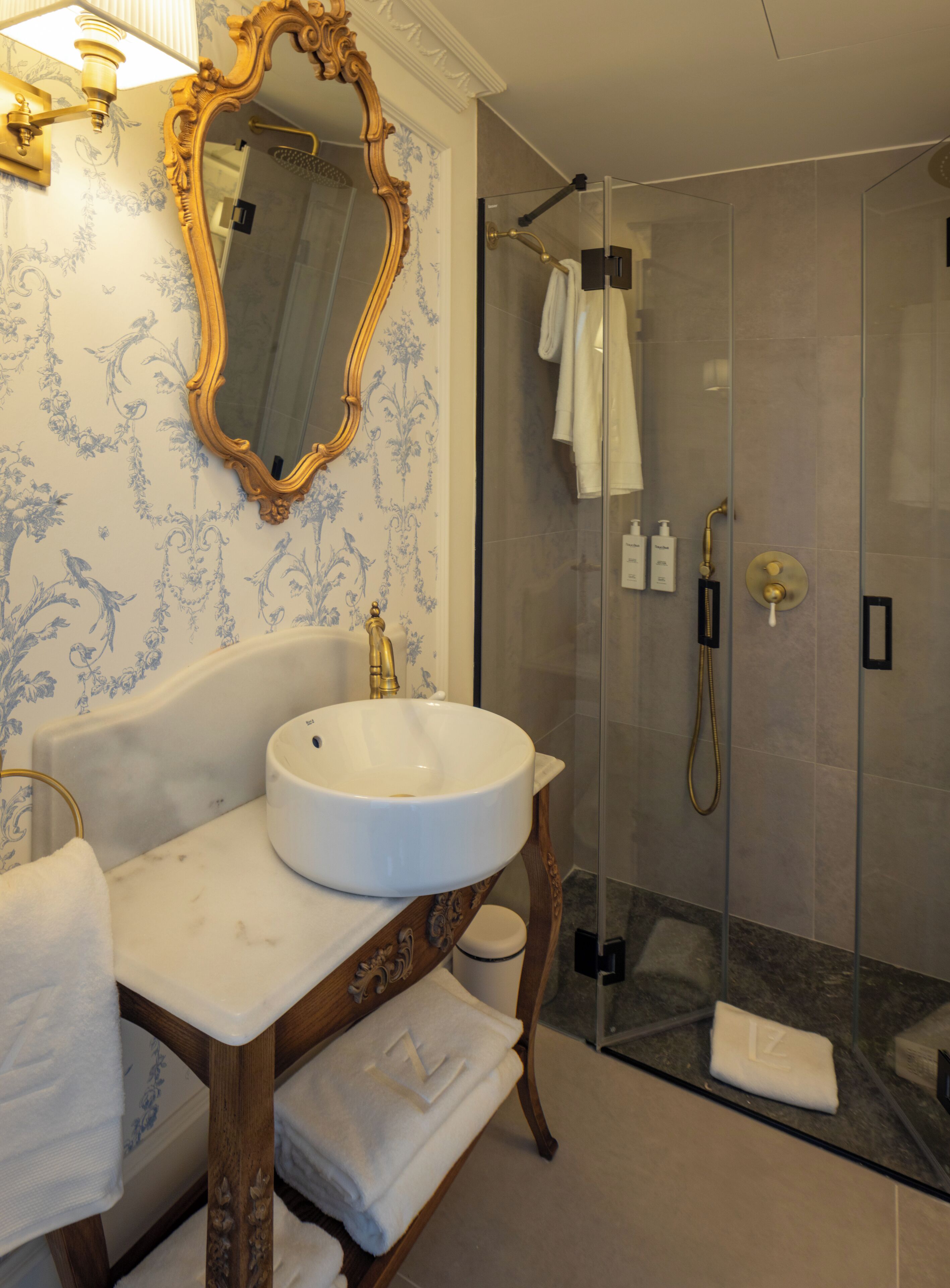 A bathroom with a marble sink, a gold-framed mirror, and a glass-enclosed shower.