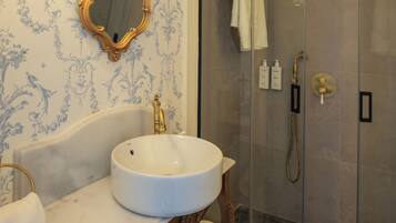 A bathroom with a marble sink, a gold-framed mirror, and a glass-enclosed shower.