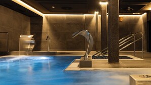 Una piscina coperta moderna con pavimento blu, un elemento d'acqua centrale e una scala che conduce a un livello superiore.