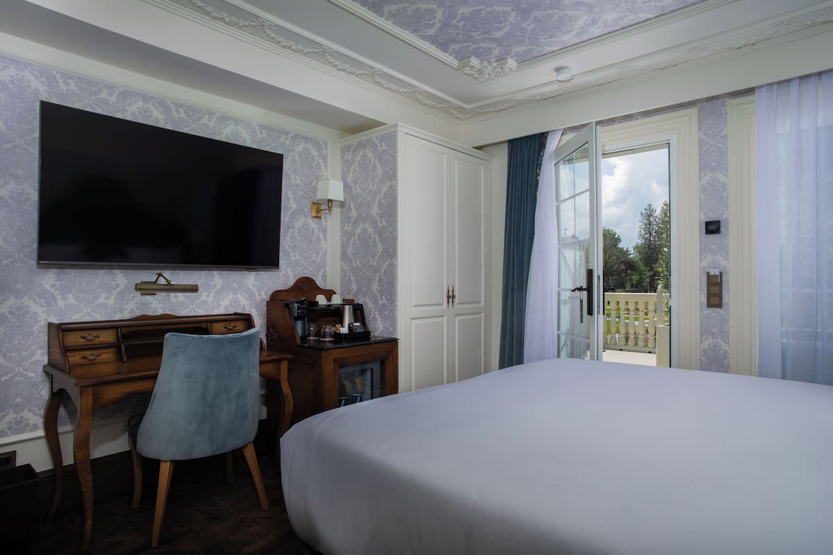 Habitación de hotel con una cama grande, un escritorio con silla, un televisor de pantalla plana y vistas al exterior a través de una puerta de cristal.