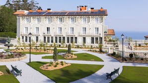 Un grande edificio a più piani con una facciata simmetrica, un cortile centrale con una fontana e vista sul mare.