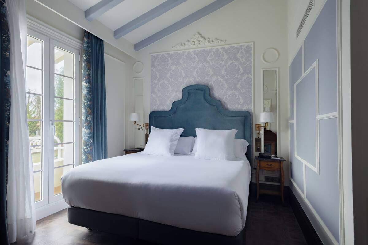 Una cama grande con cabecera azul, ropa de cama blanca y una mesita de noche con lámpara.