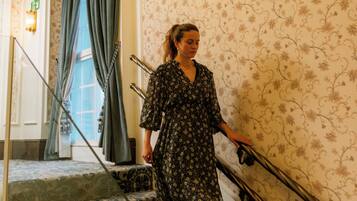 A woman descending a staircase with ornate railings and patterned wallpaper.
