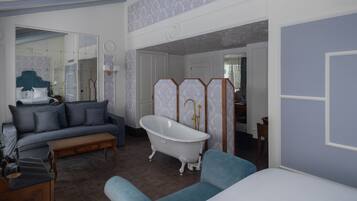 A room with a blue sofa, a wooden coffee table, a white bathtub, and a mirror.