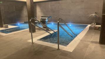 Una piscina interior con agua cristalina, barandales de metal y suelo de baldosas.