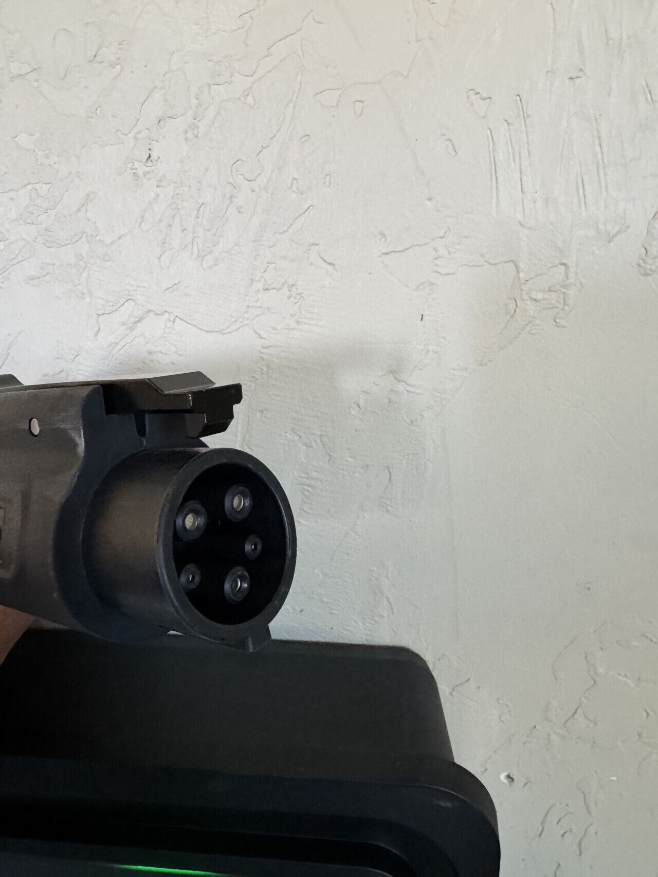 A close-up of a black electrical plug with four prongs, mounted on a white textured wall.