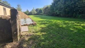 Une cour arrière verdoyante, avec une clôture en bois, un mur de pierre et un ciel bleu dégagé.