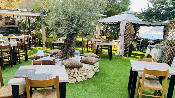 An outdoor dining area with tables and chairs, surrounded by a stone wall and greenery. - Hotel Sa Lumenera (Magomadas)