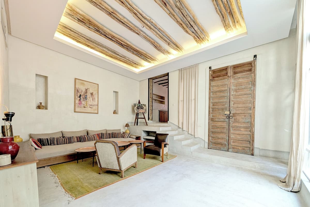 A modern living room with a sofa, armchairs, a coffee table, and a staircase leading to a wooden door.