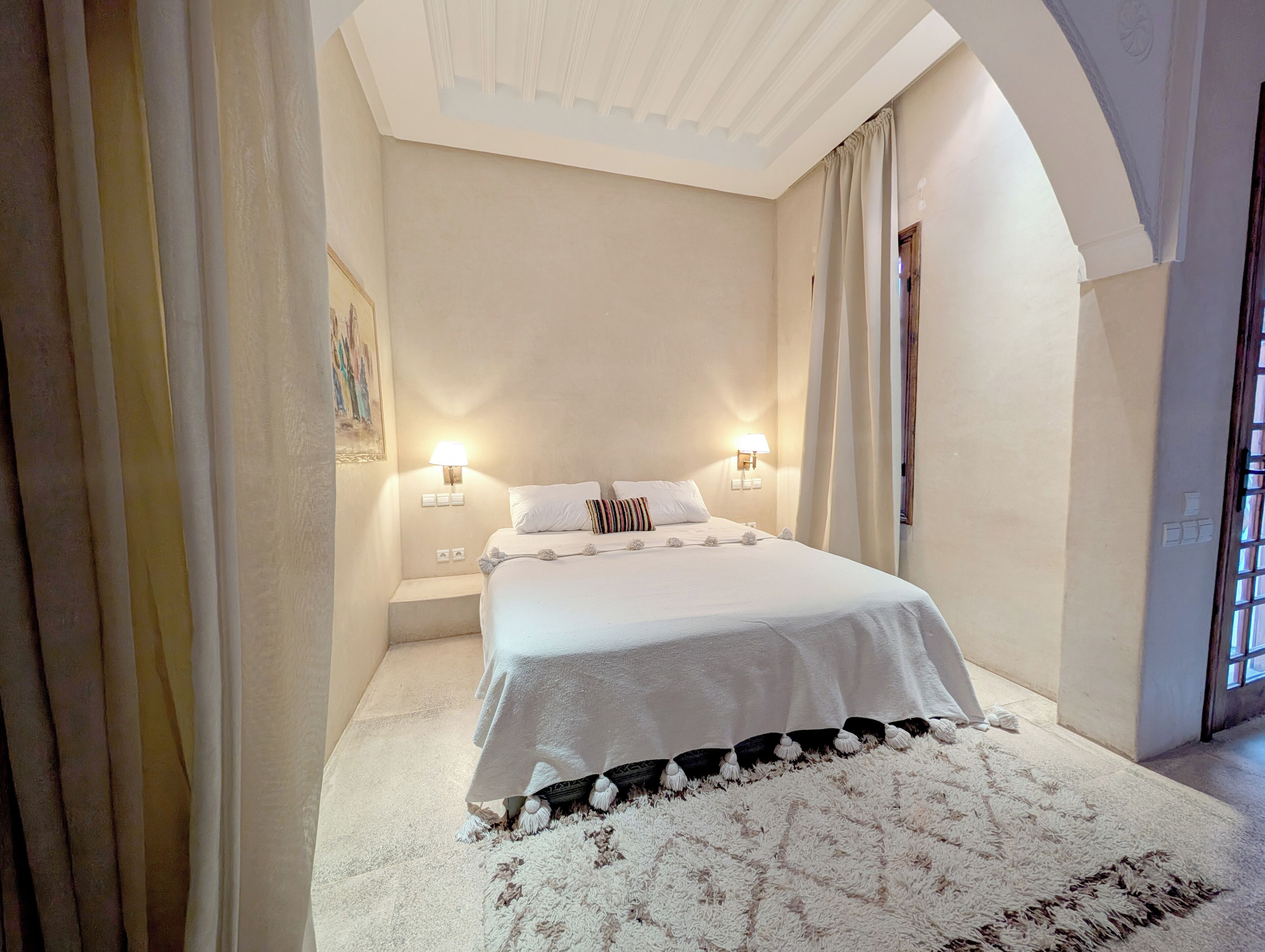 Un dormitorio con una cama grande, dos lámparas de noche, una alfombra mullida y un cuadro en la pared.