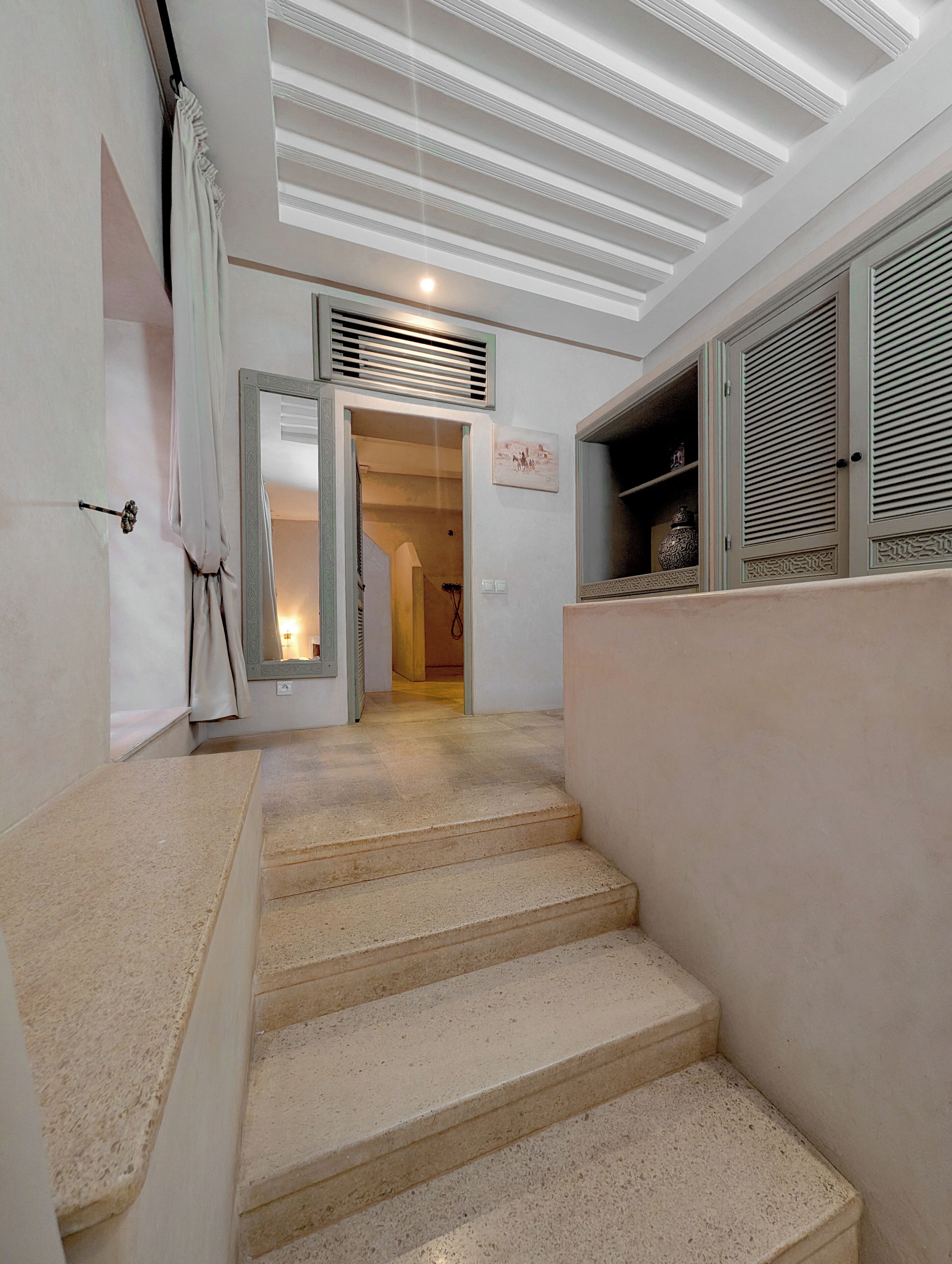 Eine Treppe führt zu einem Raum mit Deckenventilator, einer Vorhang verdeckten Tür und einem an der Wand befestigten Regal mit Dekorationen.