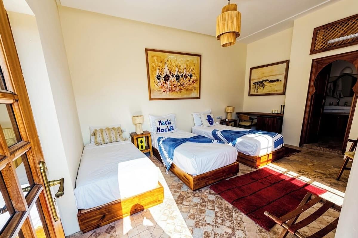 A hotel room with three beds, a wooden floor, a red rug, and artwork on the walls.