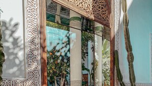 Un espace de détente de style marocain traditionnel, agrémenté de sculptures complexes en bois, d’un banc avec des coussins et d’un grand cactus en pot.
