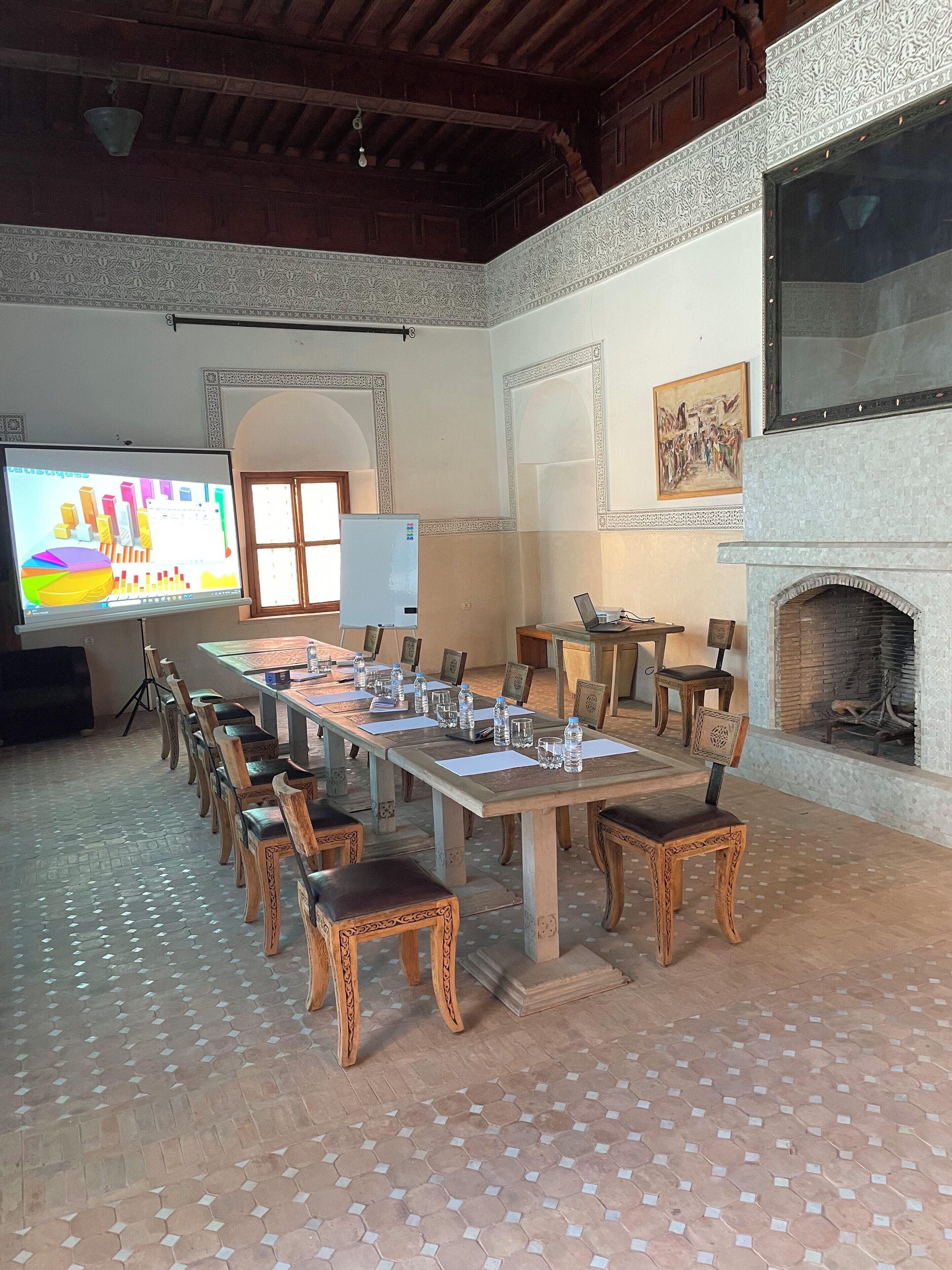 A conference room with a long table, chairs, a projector screen, and a fireplace.