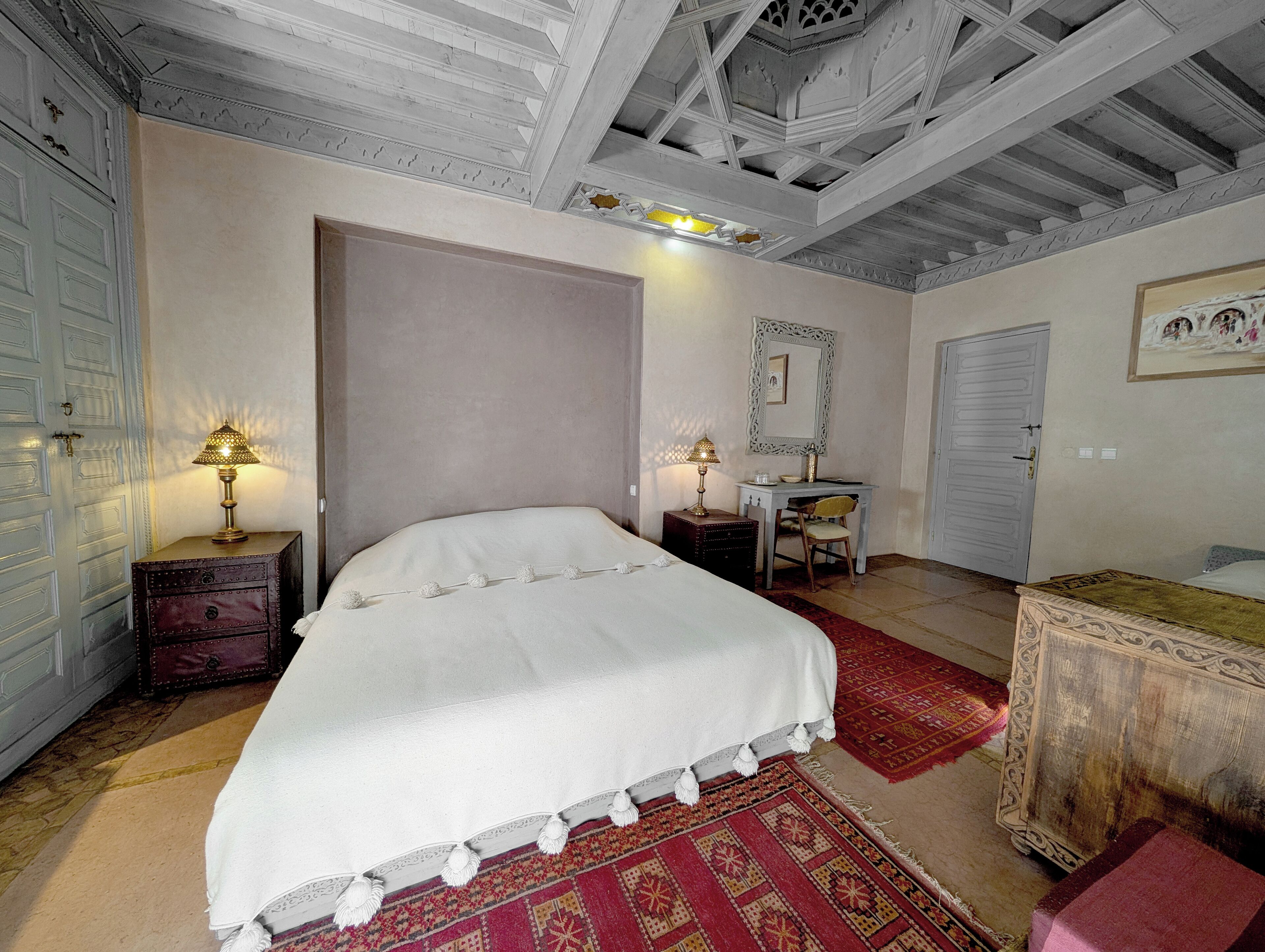 A bedroom with a large bed, a desk, a chair, a dresser, and a mirror.