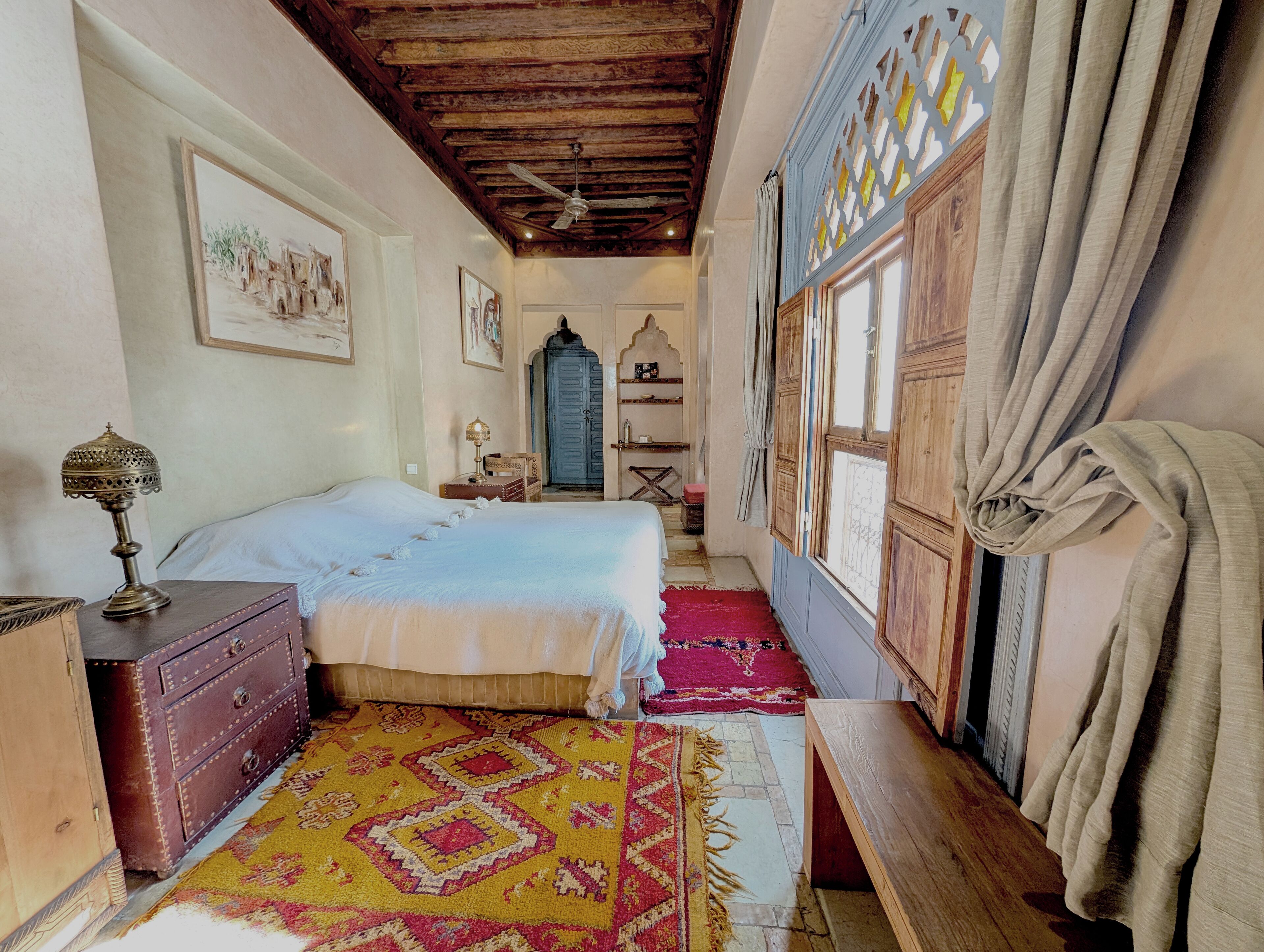 A traditional room with two beds, a wooden chest of drawers, a patterned rug, and a ceiling fan.