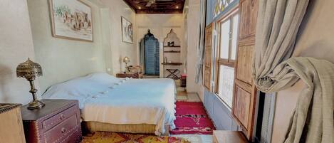 A traditional room with two beds, a wooden chest of drawers, a patterned rug, and a ceiling fan.
