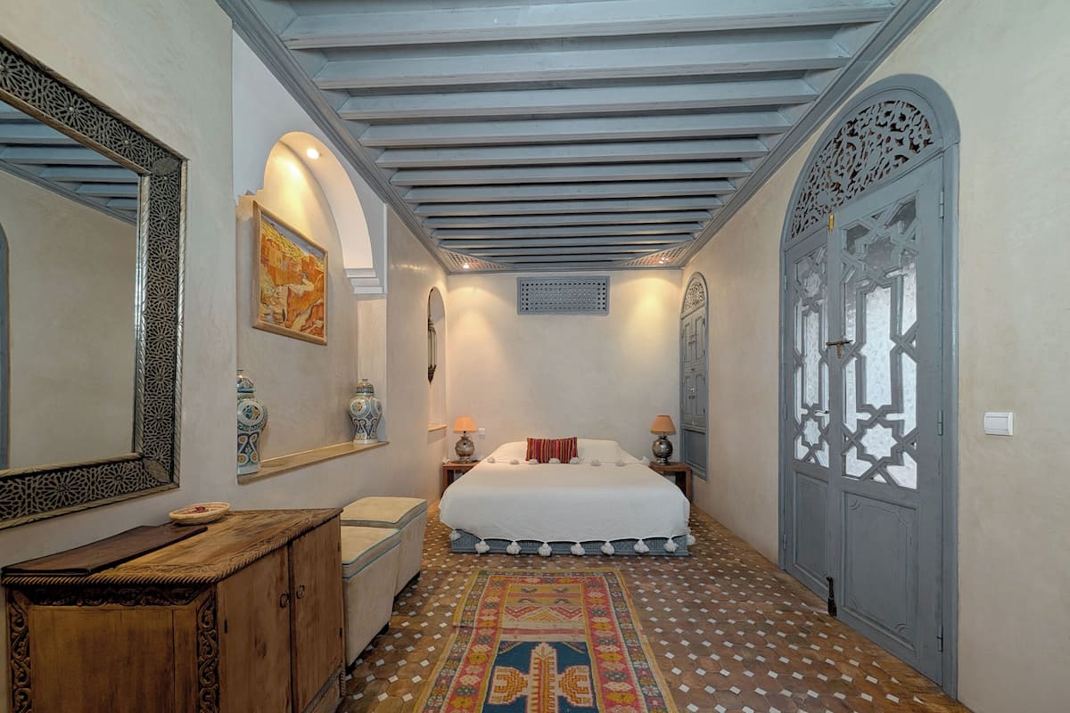 A bedroom with a large bed, a wooden dresser, a patterned rug, and a decorative door.