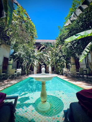 A courtyard with a central pool, surrounded by seating areas and lush greenery. - Riad Slitine (Marrakech)