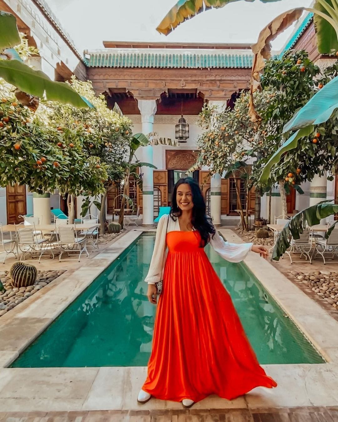 Una mujer con un vestido rojo está de pie junto a una piscina, con un edificio al fondo.