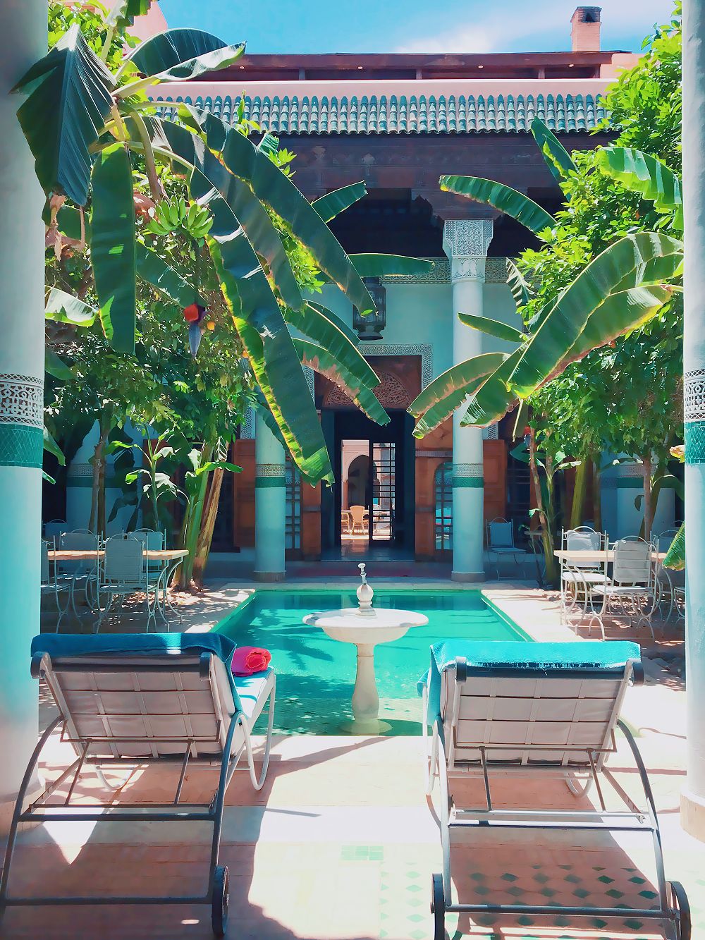 Un espace piscine agrémenté de chaises longues et d’une fontaine, le tout entouré de plantes tropicales et agrémenté d’éléments architecturaux.