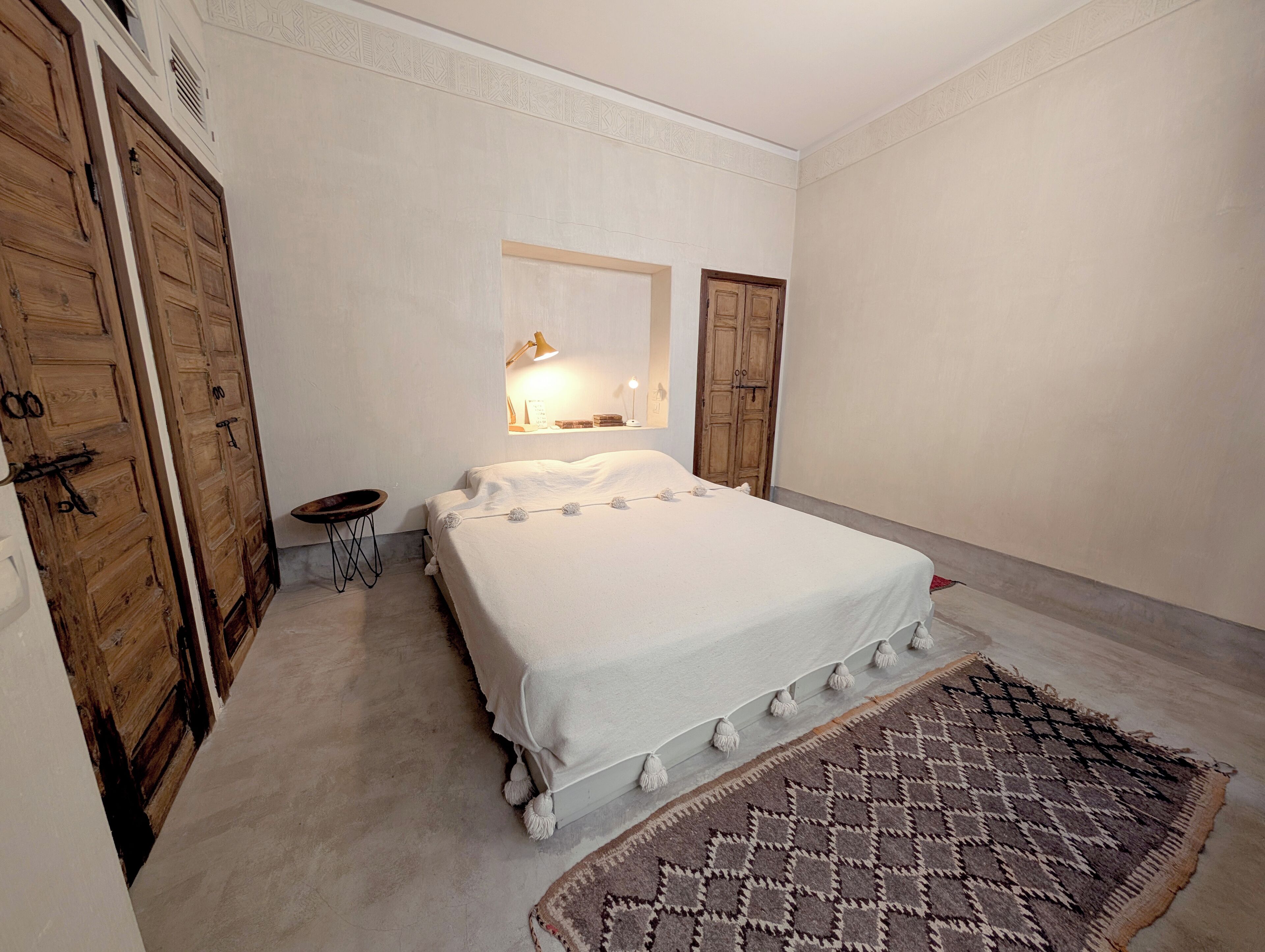 Ein Schlafzimmer mit einem großen Bett, einem Holzschrank, einem kleinen Tisch und einem gemusterten Teppich.