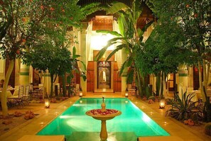 A pool area with a fountain, surrounded by lush greenery and traditional architecture. - Riad Slitine (Marrakech)