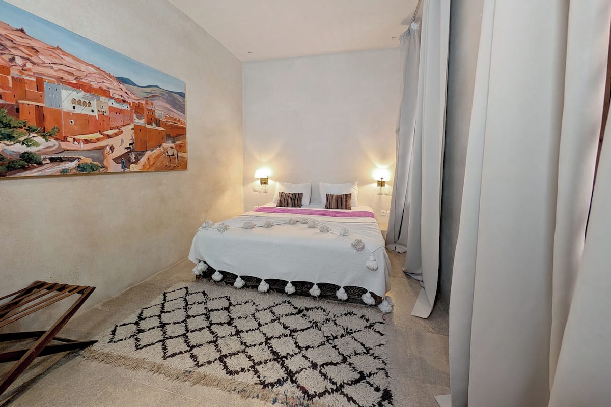 A bedroom with a bed, two bedside tables, a painting on the wall, and a patterned rug.