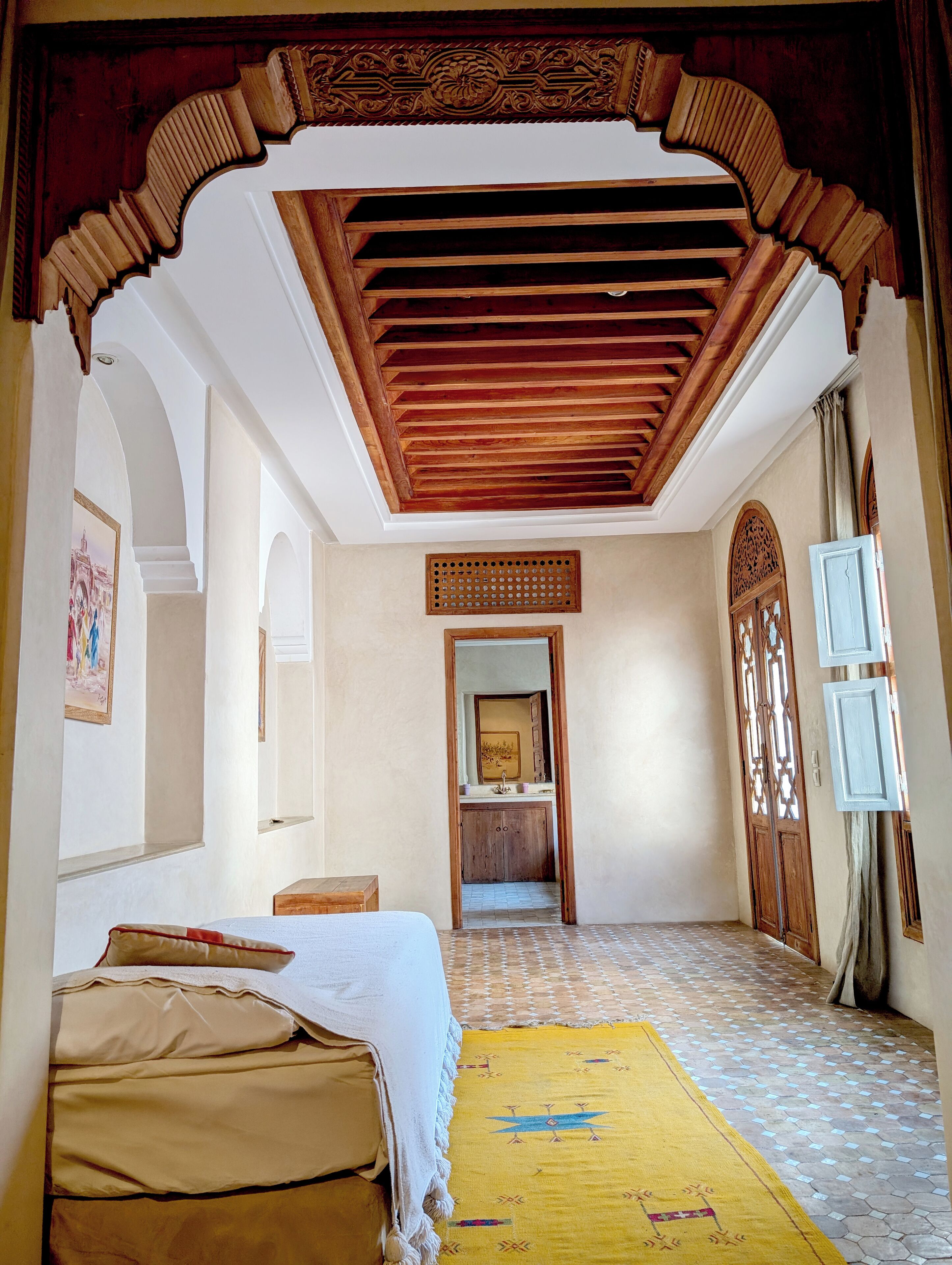A room with a bed, a wooden ceiling, a patterned floor, and a door with decorative panels.