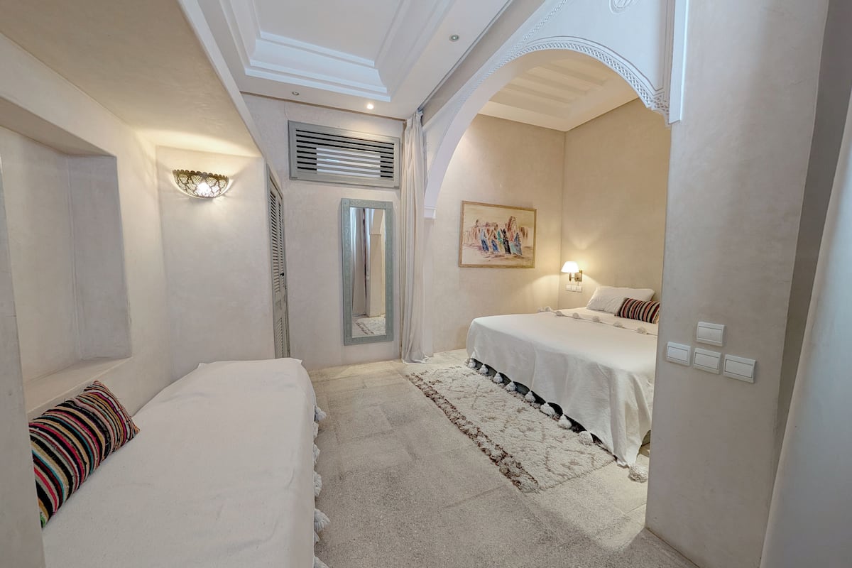 A hotel room with two beds, a large mirror, a painting on the wall, and a ceiling with decorative molding.