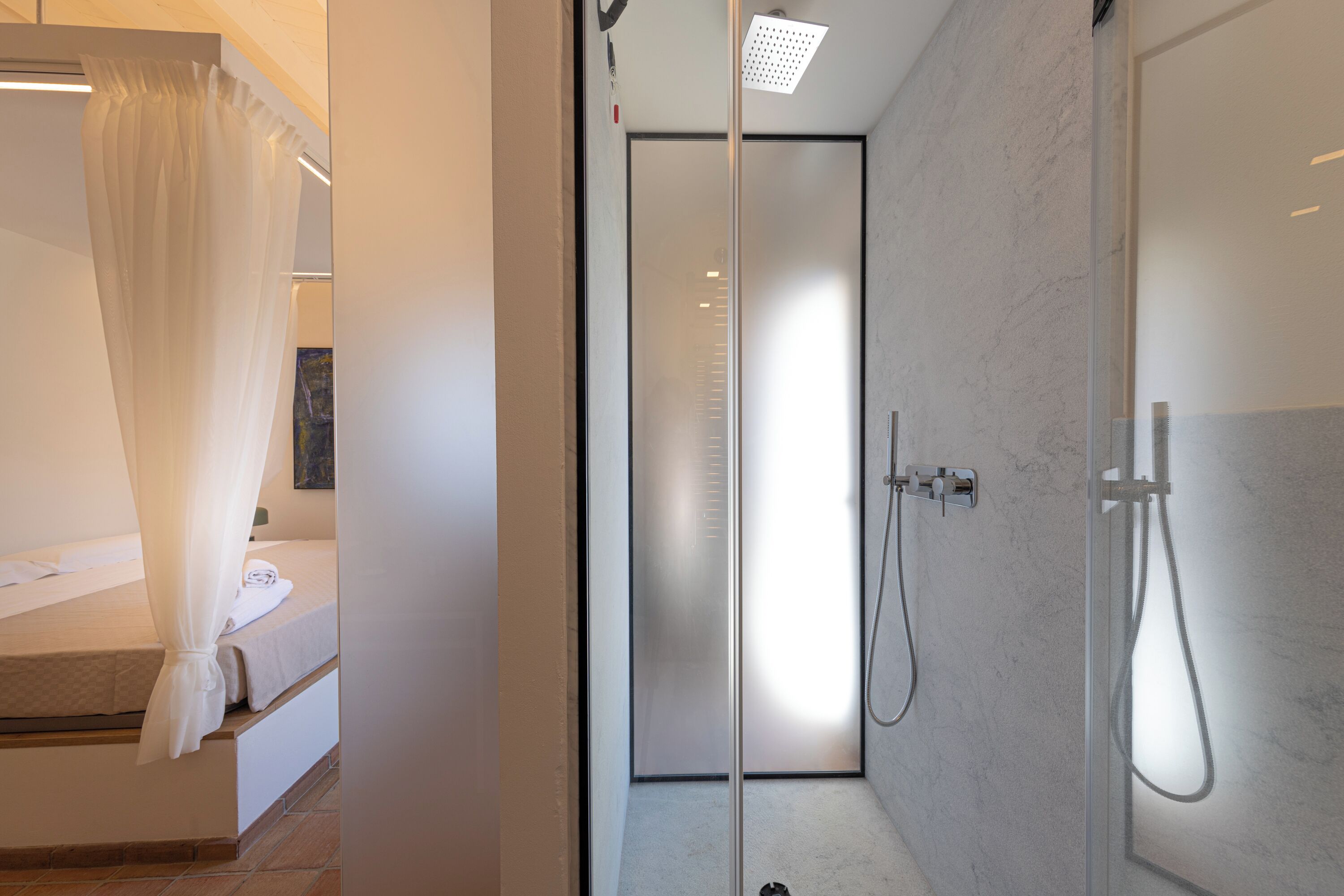 Un baño moderno con cabina de ducha de vidrio, cama con dosel y pared de mármol.